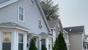 A two-story house with a front porch, a small garden with gravel and plants, and a clear sky. - Lorenzo Inn (Boston)