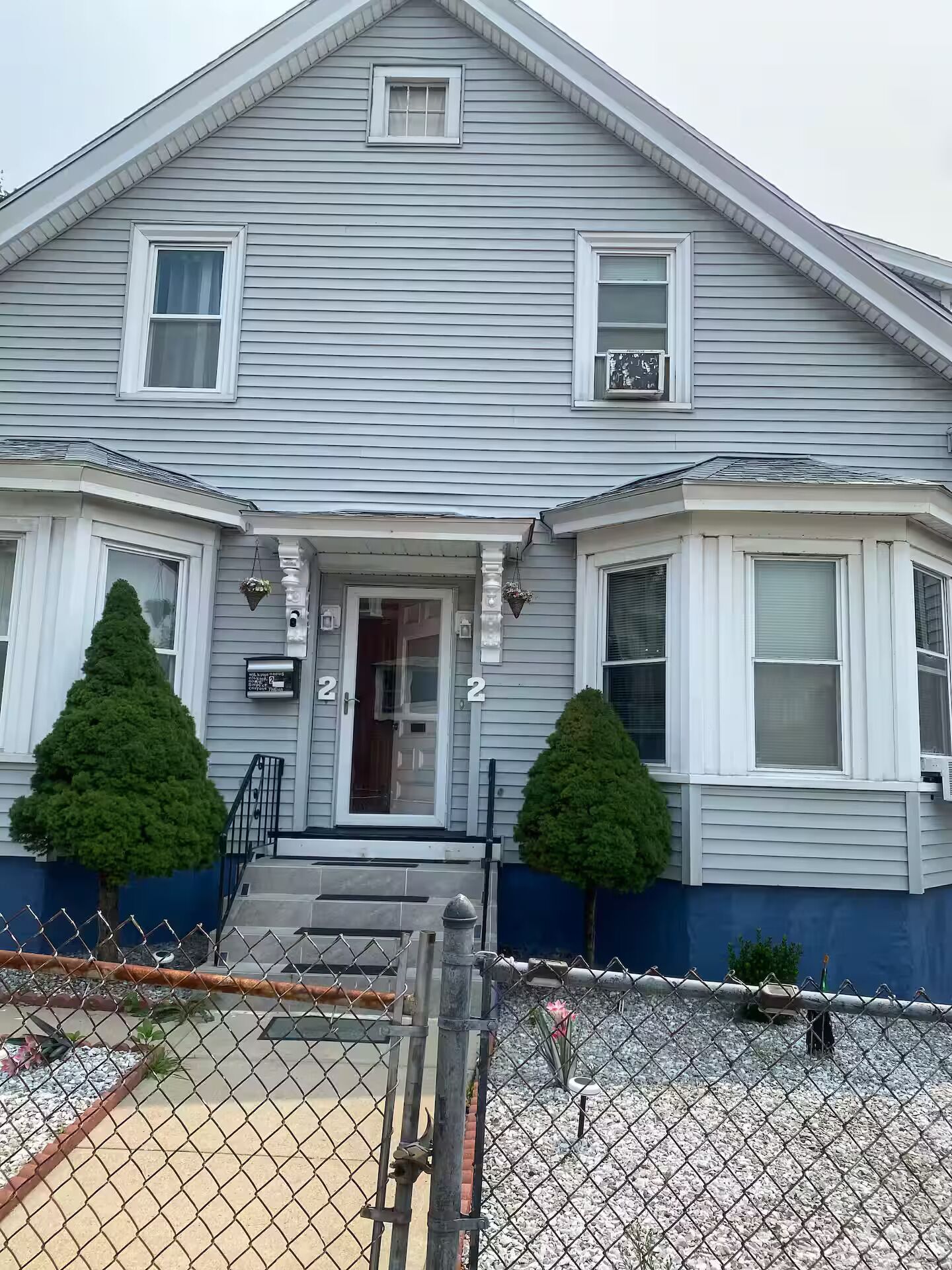 A two-story house with a front porch, two small trees, and a fenced yard.