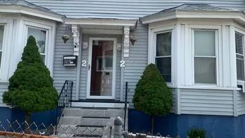 A two-story house with a front porch, two small trees, and a fenced yard.