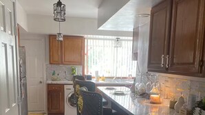 A modern kitchen with wooden cabinets, a marble countertop, and a bar area with stools. - Lorenzo Inn (Boston)