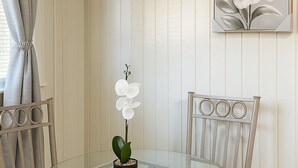 A dining area with a glass table surrounded by cushioned chairs, a potted orchid, and a wall-mounted flower painting. - Superb studio with coastal comfort in Apollo Beach, Florida (Apollo Beach)