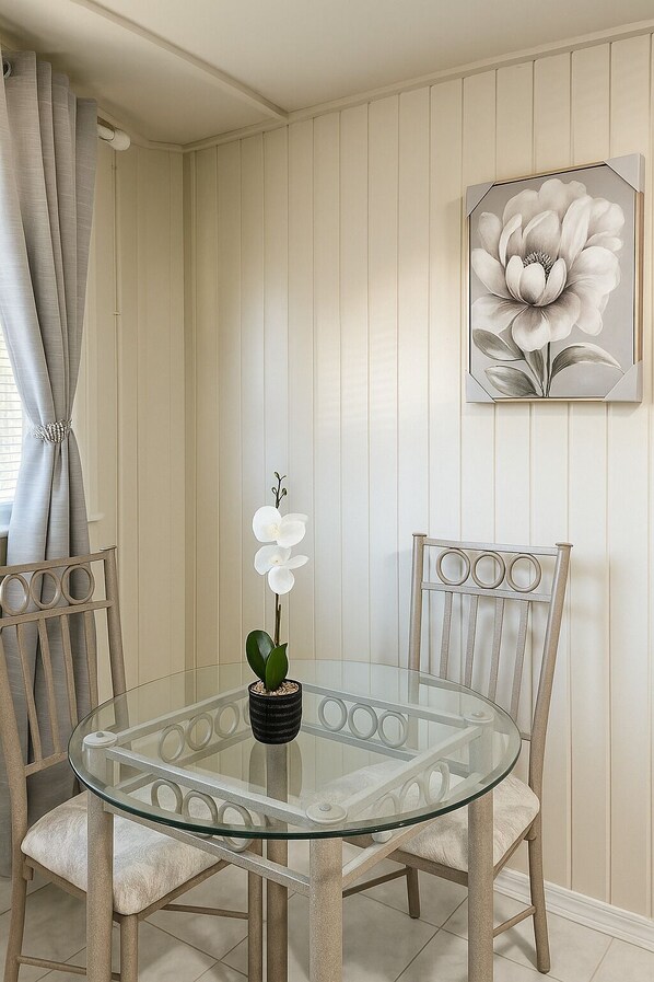 Ein Essbereich mit einem Glastisch, umgeben von gepolsterten Stühlen, einer Topf-Orchidee und einem floralen Wandbild.
