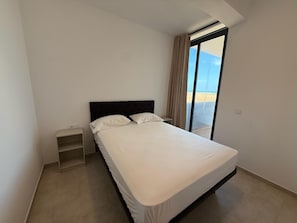 A bedroom with a bed, a nightstand, and a view of the beach through a large window. - Joli Beach House - Third Floor T3 Apartment With Beautiful Views (Sal)