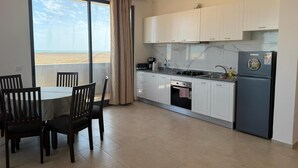 A modern kitchen with white cabinets, a built-in oven, a refrigerator, and a dining area with a table and chairs. - Joli Beach House - Third Floor T3 Apartment With Beautiful Views (Sal)