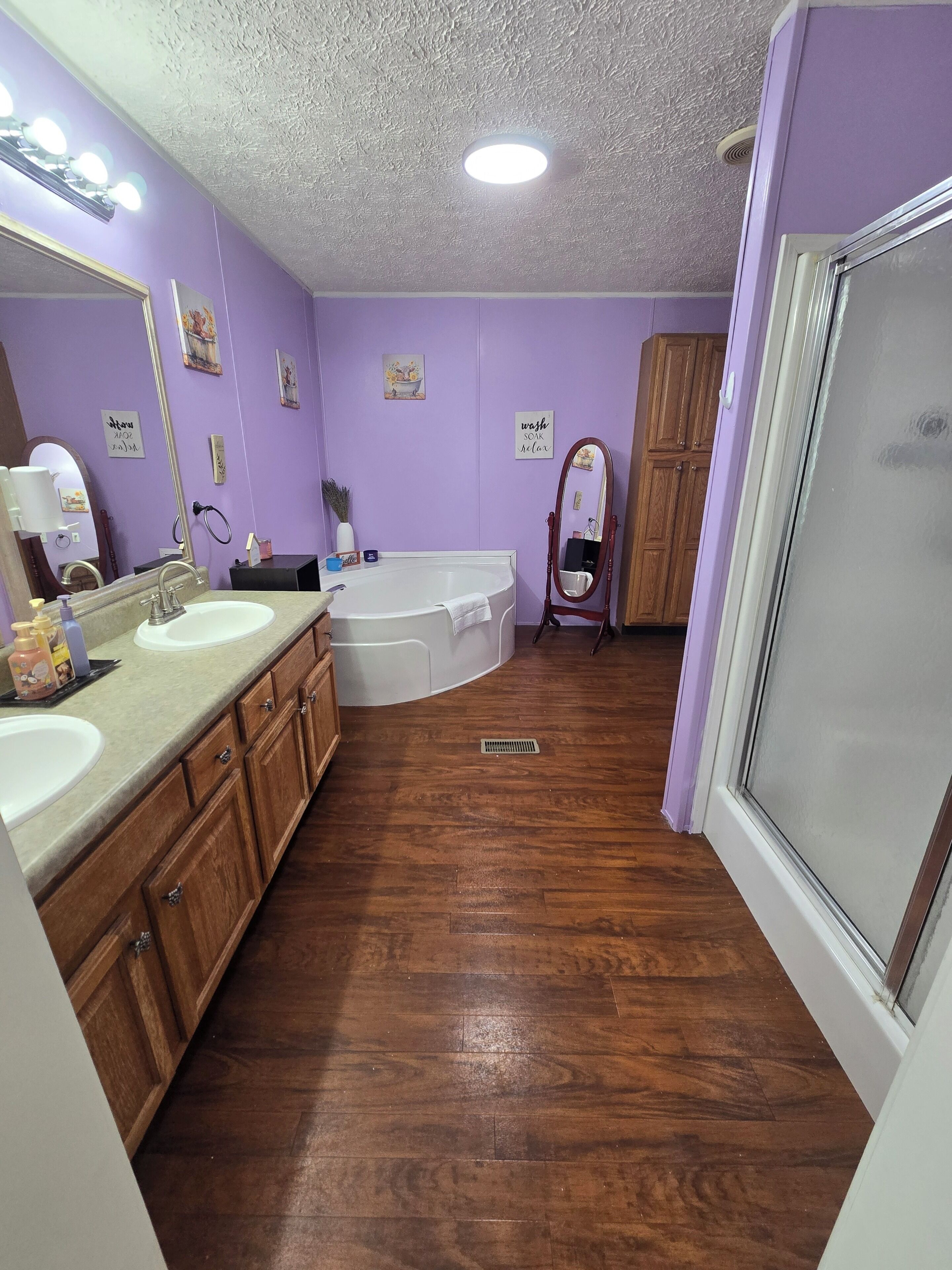 A bathroom with two sinks, a bathtub, wooden cabinets, a mirror, and a shower.