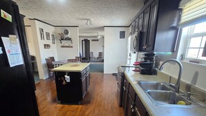 Une cuisine avec un plancher en bois, un îlot central, des meubles de couleur sombre, un évier et une fenêtre.