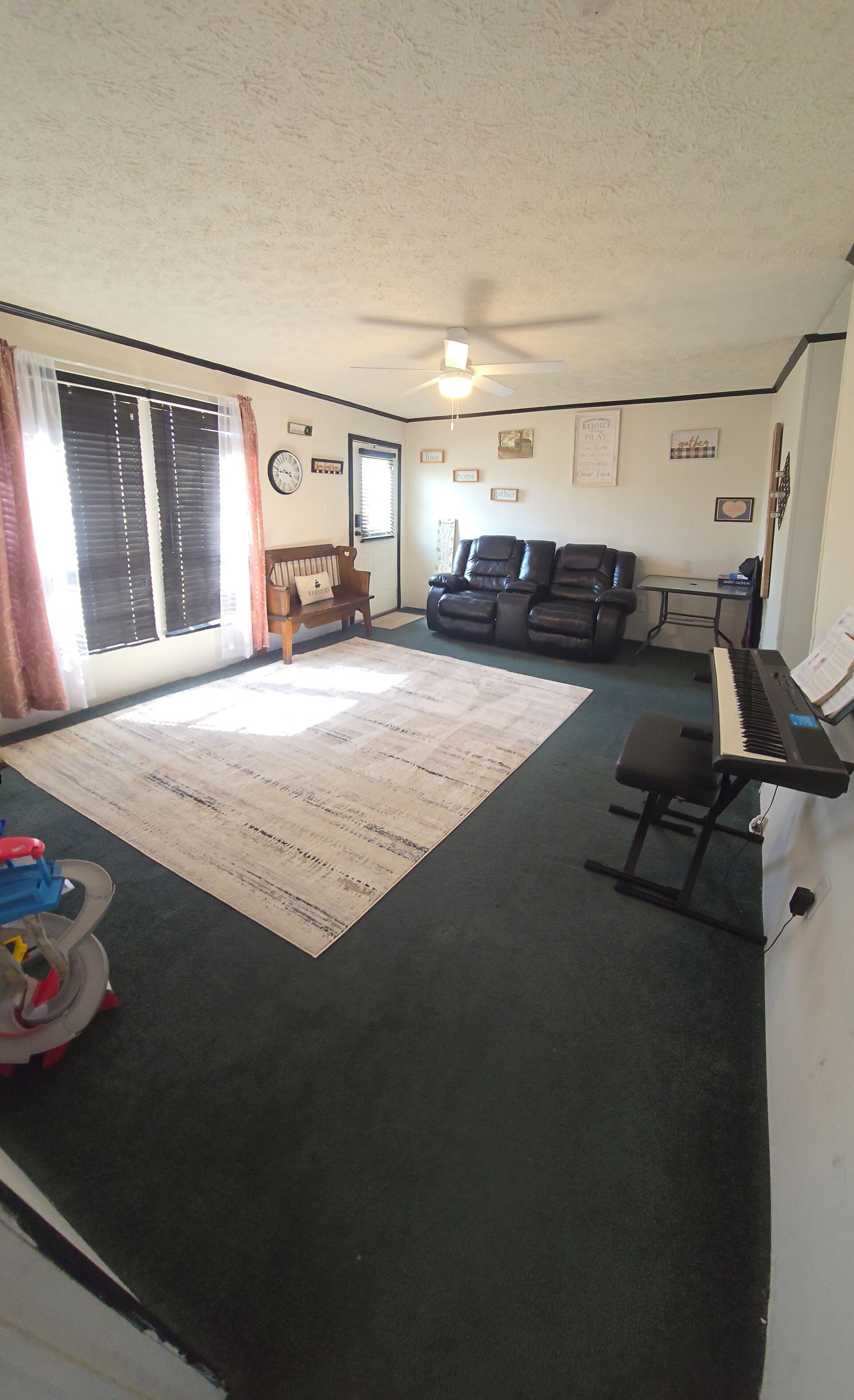 A living room with a piano, a couch, a rug, and a ceiling fan.