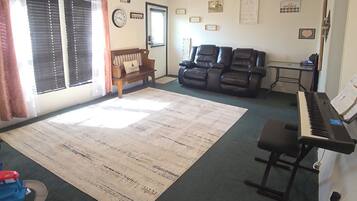 A living room with a piano, a couch, a rug, and a ceiling fan.