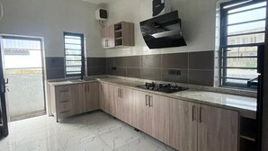 A modern kitchen with marble flooring, wooden cabinets, a built-in stove, and a window with blinds.