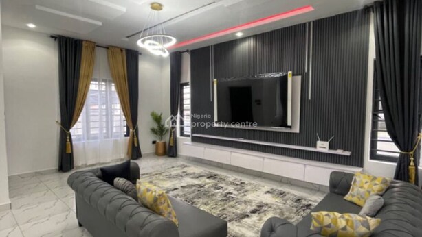 A modern living room with two grey sofas, a patterned rug, and a large TV on the wall.