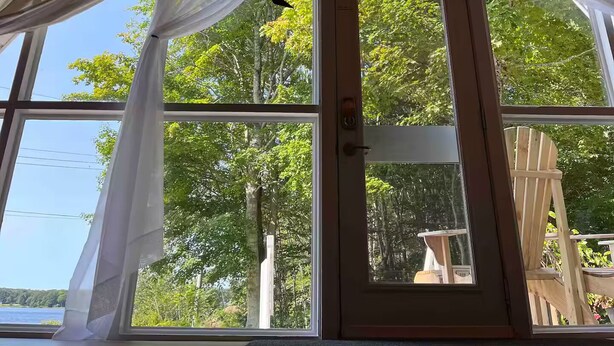 A room with a sloped ceiling, large windows, and a view of trees and a body of water. - Lakeside A-frame Cottage (Clare)