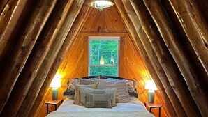 A cozy attic bedroom with a large bed, two bedside lamps, and a window with a view of trees. - Lakeside A-frame Cottage (Clare)