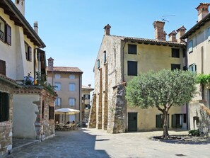 A narrow street with stone buildings, a tree, and outdoor seating. - Lovely apartment in villa for 6 people with pool, A/C, WIFI and terrace (Grado)