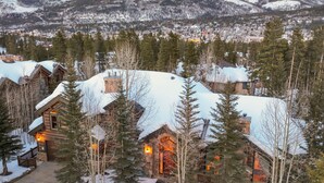 Eine schneebedeckte Lodge mit Steinaußenwand und Holzverkleidung, umgeben von Bäumen und einer Bergkulisse.