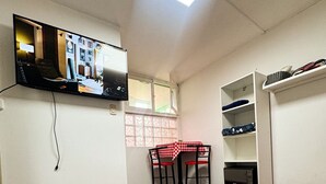 Een slaapkamer met een bed, een aan de muur bevestigde televisie, een raam met uitzicht en een kleine tafel met stoelen.