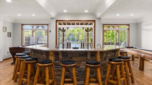 A bar area with a stone countertop, wooden stools, and large windows with a view of greenery. - Pier Pressure by PMR, Lakefront, Private Boat Slip, fire pit, gameroom (Lake Harmony)
