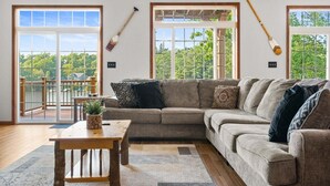 A living room with a sectional sofa, a wooden coffee table, and a view through large windows. - Pier Pressure by PMR, Lakefront, Private Boat Slip, fire pit, gameroom (Lake Harmony)