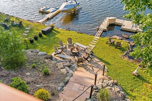 Une terrasse au bord du lac, aménagée avec du mobilier d’extérieur, un foyer et un quai avec un bateau.