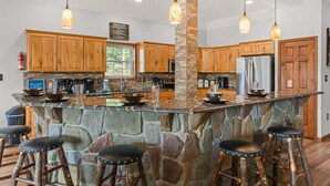 A kitchen with wooden cabinets, a stone island with stools, hanging pendant lights, and a fire extinguisher. - Pier Pressure by PMR, Lakefront, Private Boat Slip, fire pit, gameroom (Lake Harmony)