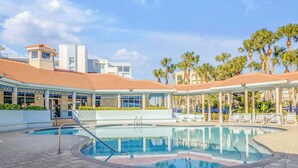 Un espace piscine doté d’une terrasse carrelée, de chaises longues et de palmiers.