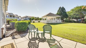 Een terras met twee groene stoelen en een tafel, een overdekte pergola en een verzorgd gazon.