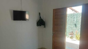 Une petite pièce simple, avec un lit, une télévision et une porte donnant sur un balcon.