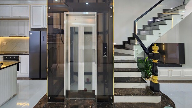 Une cuisine moderne dotée d’un réfrigérateur encastré, d’un ascenseur en verre et d’un escalier avec une rampe noire.