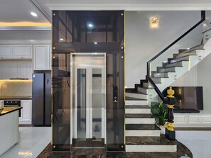 Une cuisine moderne dotée d’un réfrigérateur encastré, d’un ascenseur en verre et d’un escalier avec une rampe noire.
