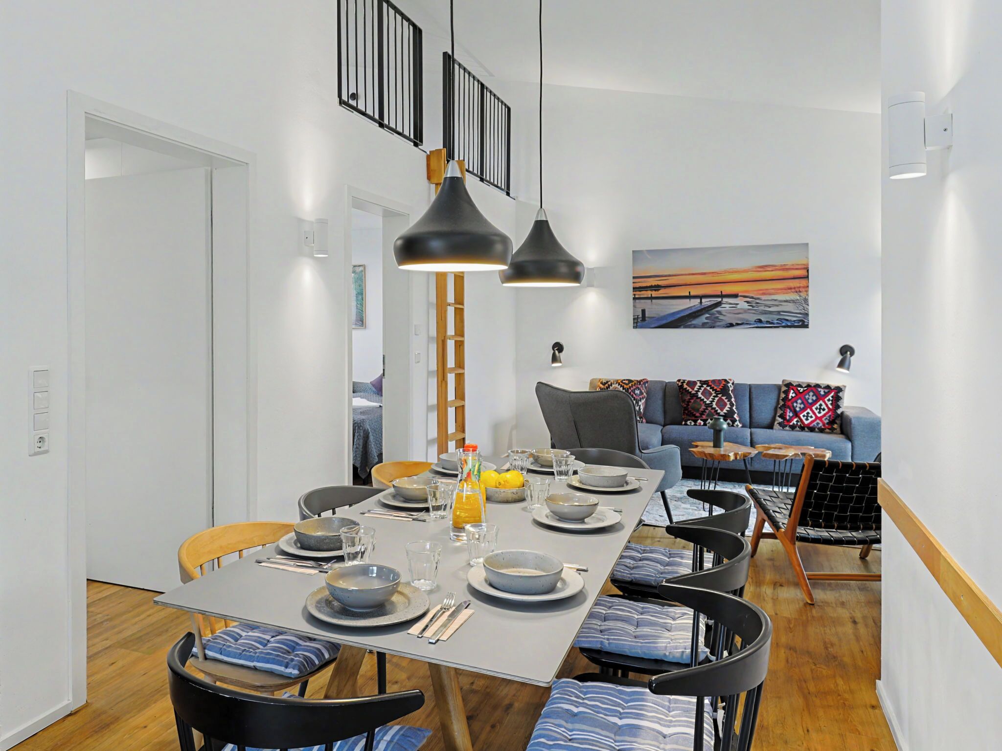 A dining area with a table set for four, chairs with blue cushions, a wooden ladder, and a blue sofa with patterned cushions.