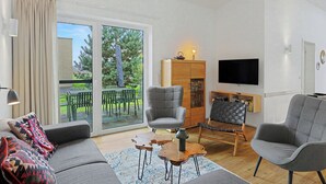 A modern living room with a sofa, two armchairs, a coffee table, a TV, and a sliding glass door leading to an outdoor patio.
