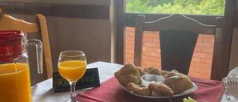 A breakfast setting with a table set for two, featuring a plate of rolled bananas, a plate of croissants, a glass of orange juice, a glass of orange juice, and a cup of coffee.
