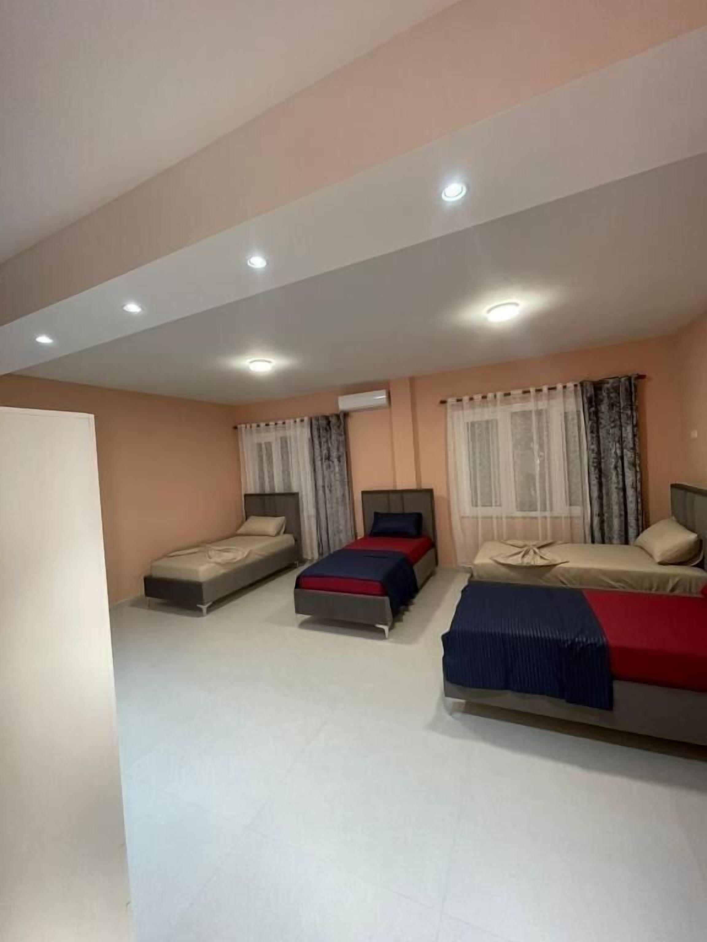A hotel room with three beds, a white ceiling, and an air conditioning unit.