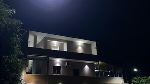 A modern two-story building with multiple balconies, large windows, and a paved entrance area.