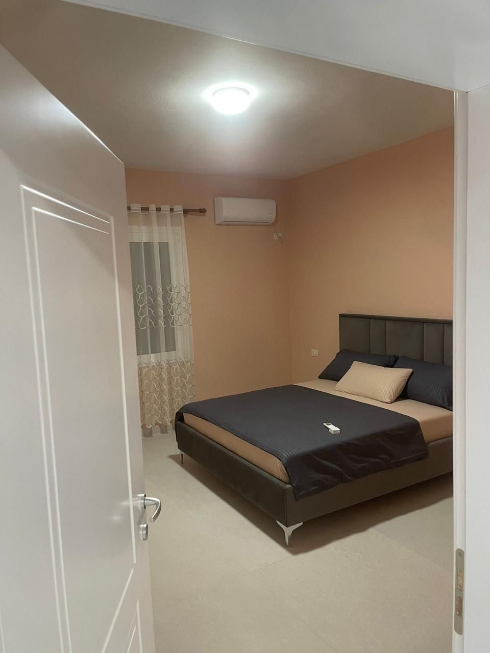 Un dormitorio con una cama, aire acondicionado, una puerta y una ventana con cortinas.