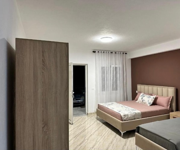 A bedroom with a bed, a wardrobe, and a door leading to a parking area.
