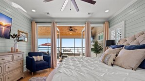 Un dormitorio con una cama grande, un sillón azul, un aparador de madera y vistas al exterior a través de un ventanal.