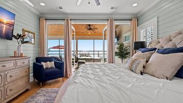 Une chambre à coucher avec un grand lit, un fauteuil bleu, une commode en bois et une vue sur l’extérieur par une grande fenêtre.