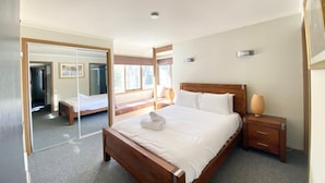 Quarto de hotel moderno com uma cama grande, uma mesinha de cabeceira de madeira, um espelho e uma janela com vista para o exterior.