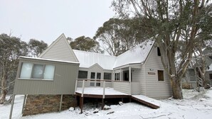 Uma casa de dois andares com base de pedra, varanda coberta e um pequeno deck.