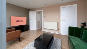 A modern living room with a flat-screen TV, a green sofa, a coffee table, and a fireplace. - GuestReady - Charming 3-Bedroom London Retreat (London)