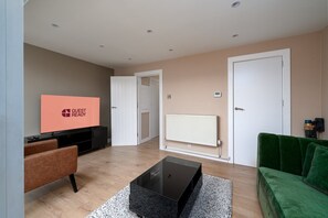 Een moderne woonkamer met een flatscreen televisie, een groene bank, een bijzettafeltje en een open haard.