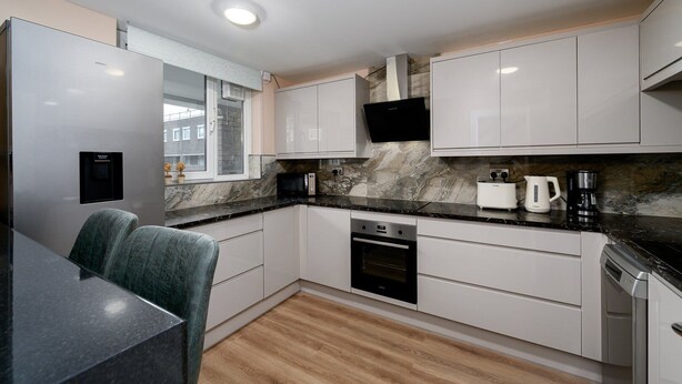 A modern kitchen with white cabinets, a built-in oven, a microwave, and a coffee maker on the countertop. - GuestReady - Charming 3-Bedroom London Retreat (London)