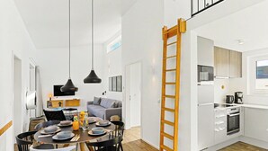 Eine moderne Küche mit weißen Schränken, einer Holzleiter und einem Essbereich mit rundem Tisch und Stühlen.