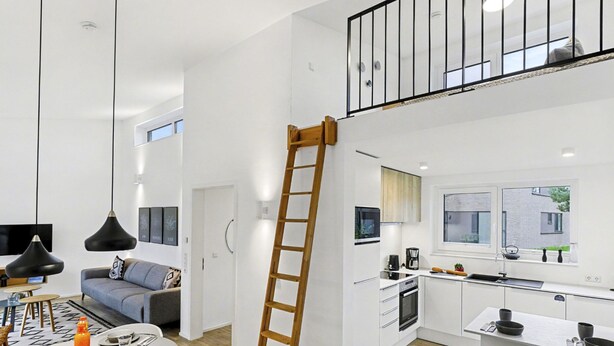 Une cuisine moderne dotée d’un îlot central, un coin repas avec une table ronde et une chambre à coucher de style loft avec balcon.