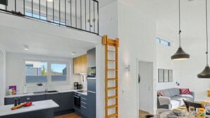 Una cocina moderna con una isla central, un comedor con mesa dispuesta para cuatro personas y un dormitorio tipo loft con balcón.