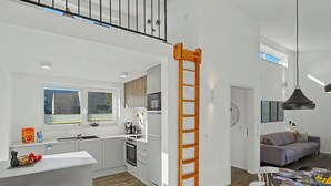Uma cozinha moderna com ilha central, área de refeições com mesa posta para quatro e escada que leva a um andar superior.
