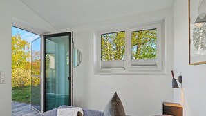 Um quarto com uma cama, duas janelas, uma porta para uma varanda e uma mesa de cabeceira com abajur.