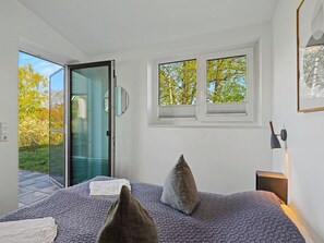 Une chambre à coucher avec un lit, deux fenêtres, une porte donnant sur un balcon et une table de chevet avec une lampe.