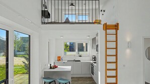Cozinha moderna com ilha central, dois banquetes, uma escada de madeira e vista para o exterior.