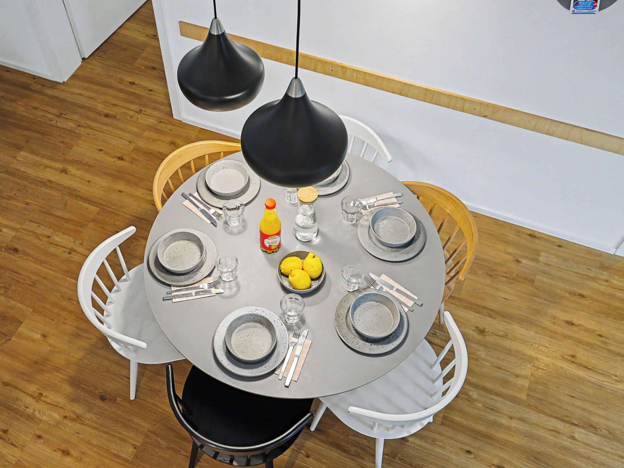 A round dining table with plates, cutlery, glasses, and a lemon bowl.
